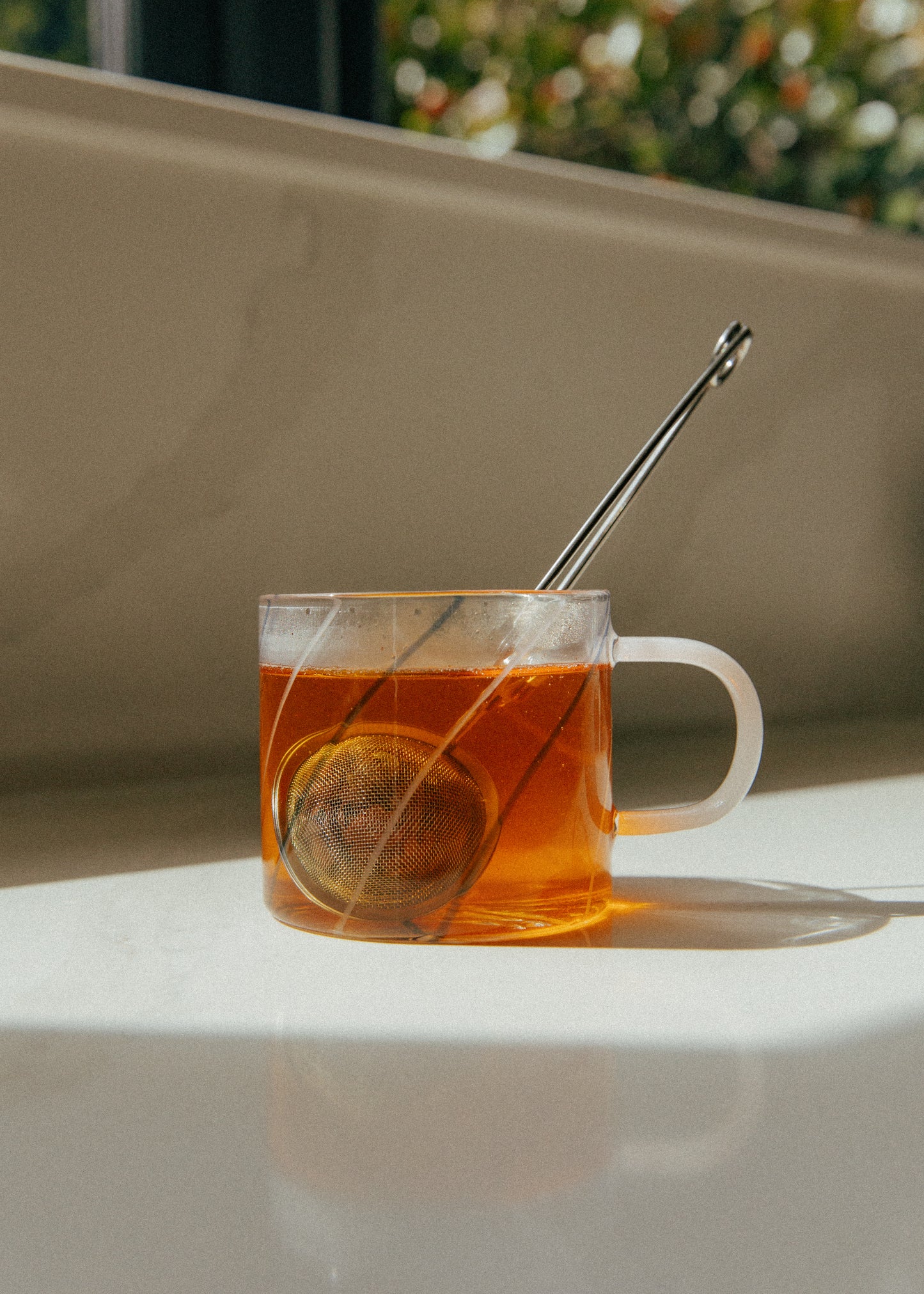 Clear mug with cacao tea and a tea ball on a white surface with a blurred green background