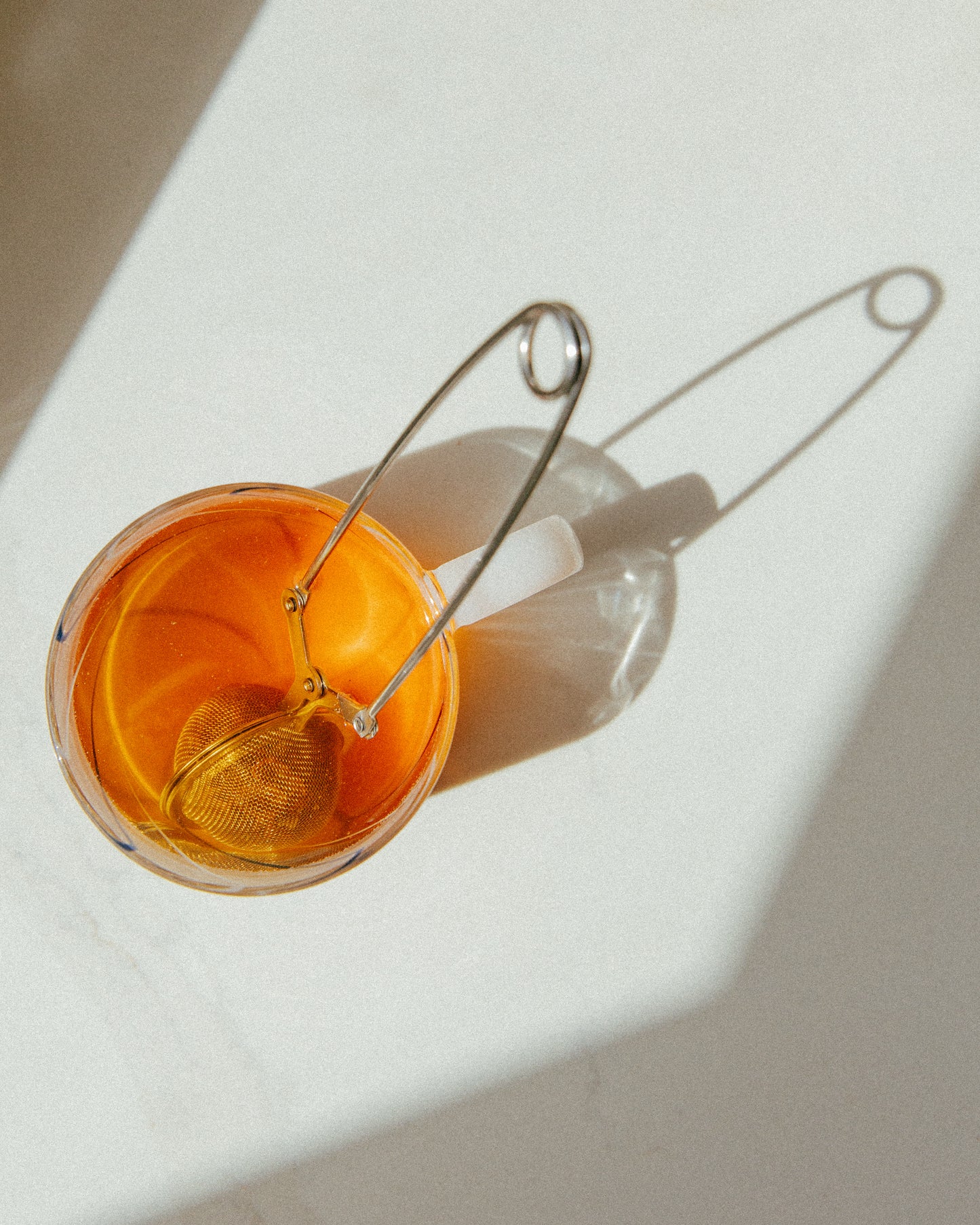 Glass with cacao husk tea and a metal strainer on a white surface